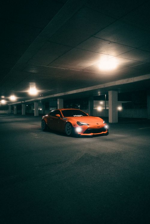 Free Orange sportscar parked in a dimly lit underground garage at night, showcasing automotive allure. Stock Photo