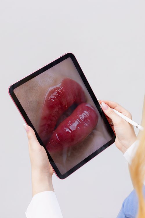 Free A person holding a tablet with vivid lip art displayed on the screen in an artistic, modern setting. Stock Photo