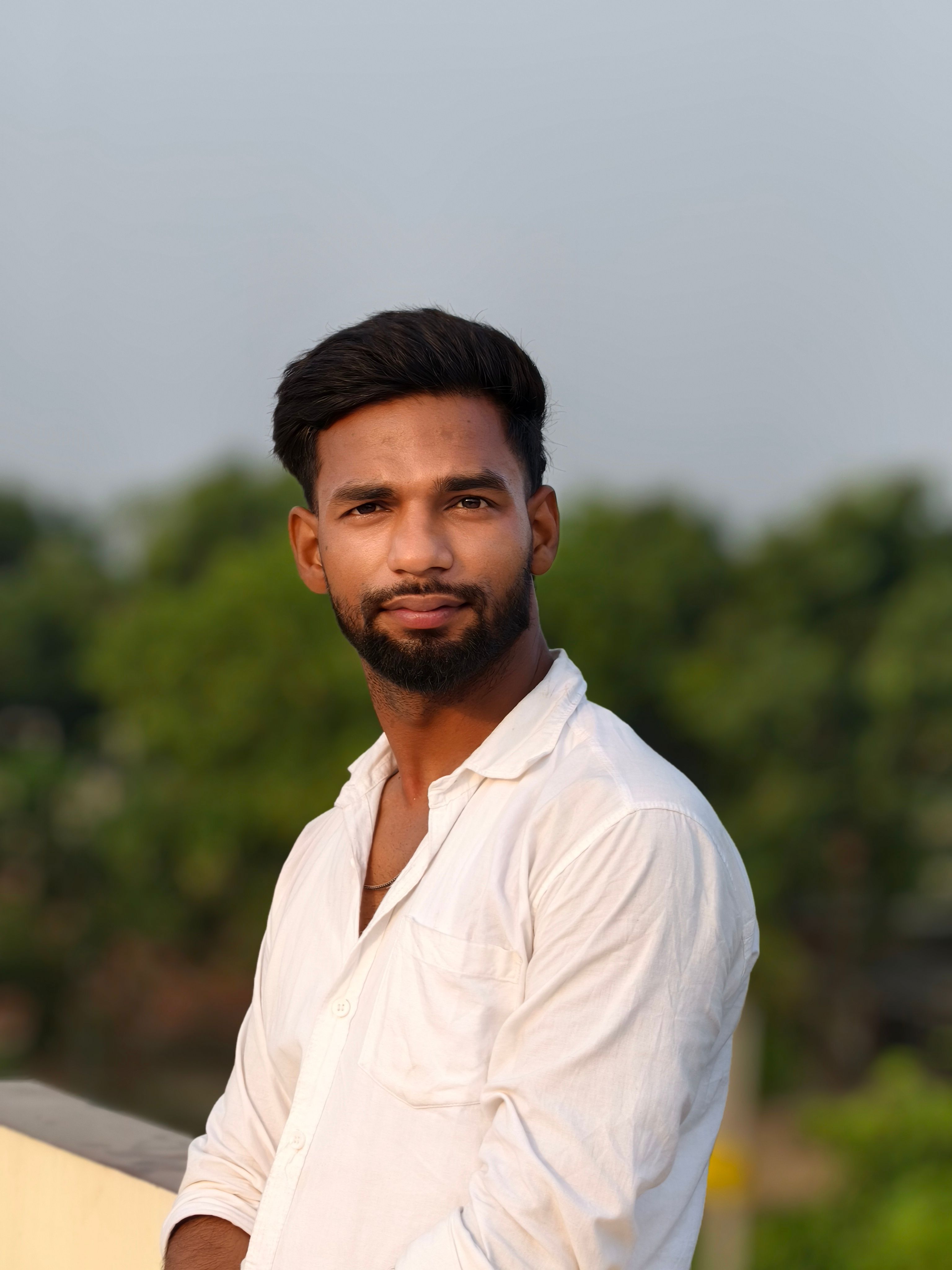 Portrait of a confident young man standing outdoors in casual attire, with a natural background.