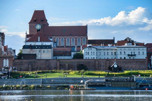 Free Scenic view of Toruń's Gothic architecture along the Vistula River on a sunny day, capturing historical charm. Stock Photo