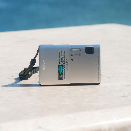 Free Close-up of a silver digital camera resting on a marble surface with a blue background. Stock Photo
