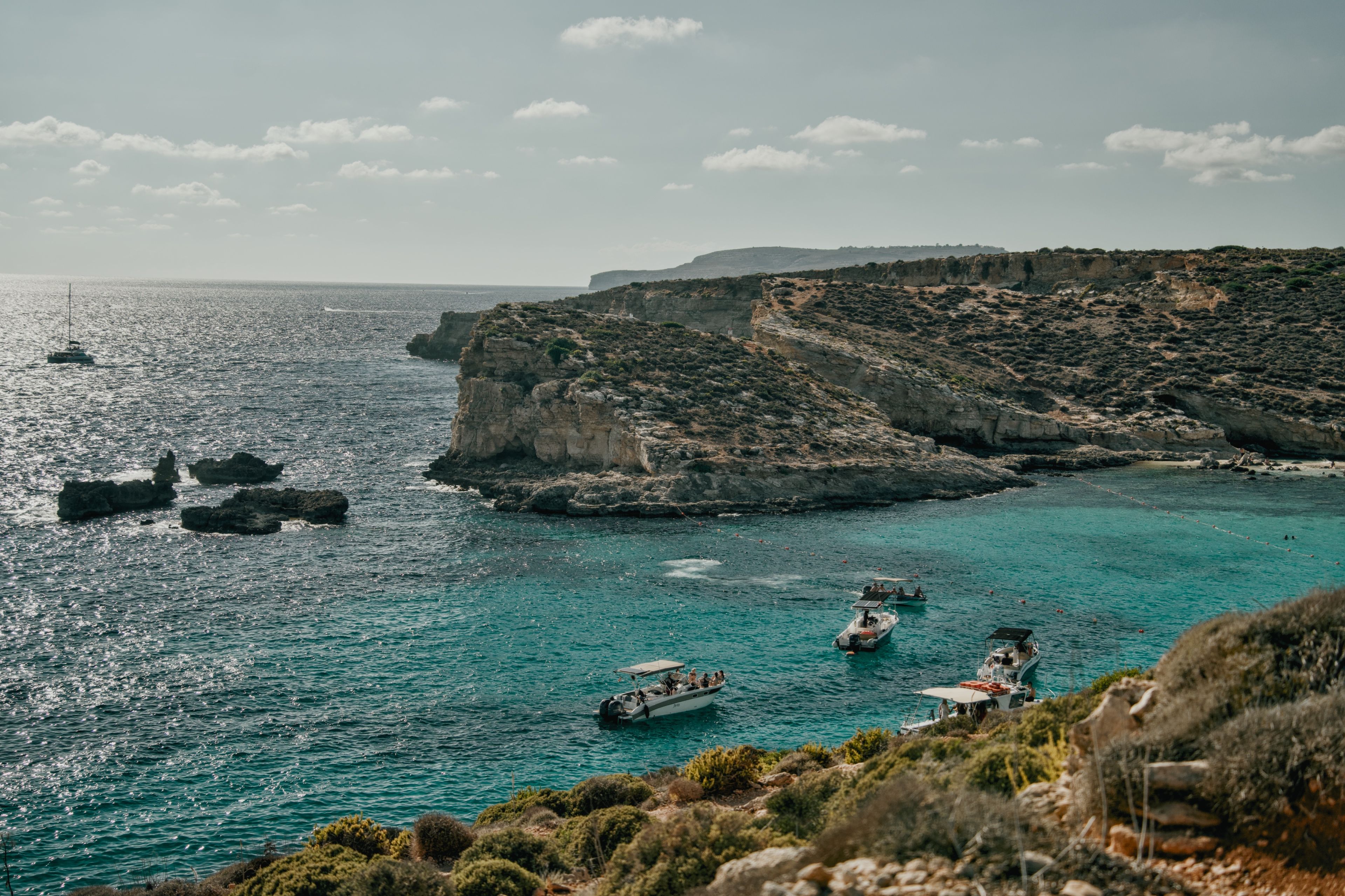 A breathtaking view of Malta's coastline featuring turquoise waters, boats, and limestone cliffs under a clear sky. - Photo by Dawid Tkocz on Pexels