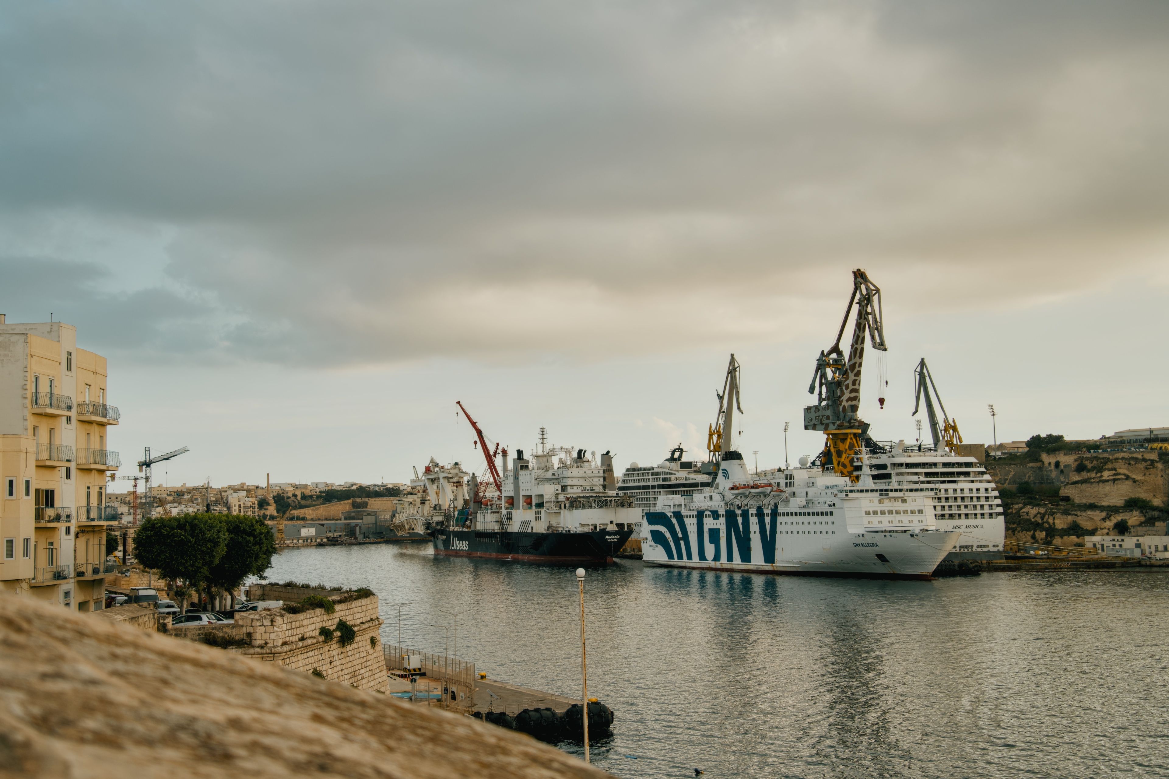 A dockside view of ferries and cranes at an industrial port in Malta.