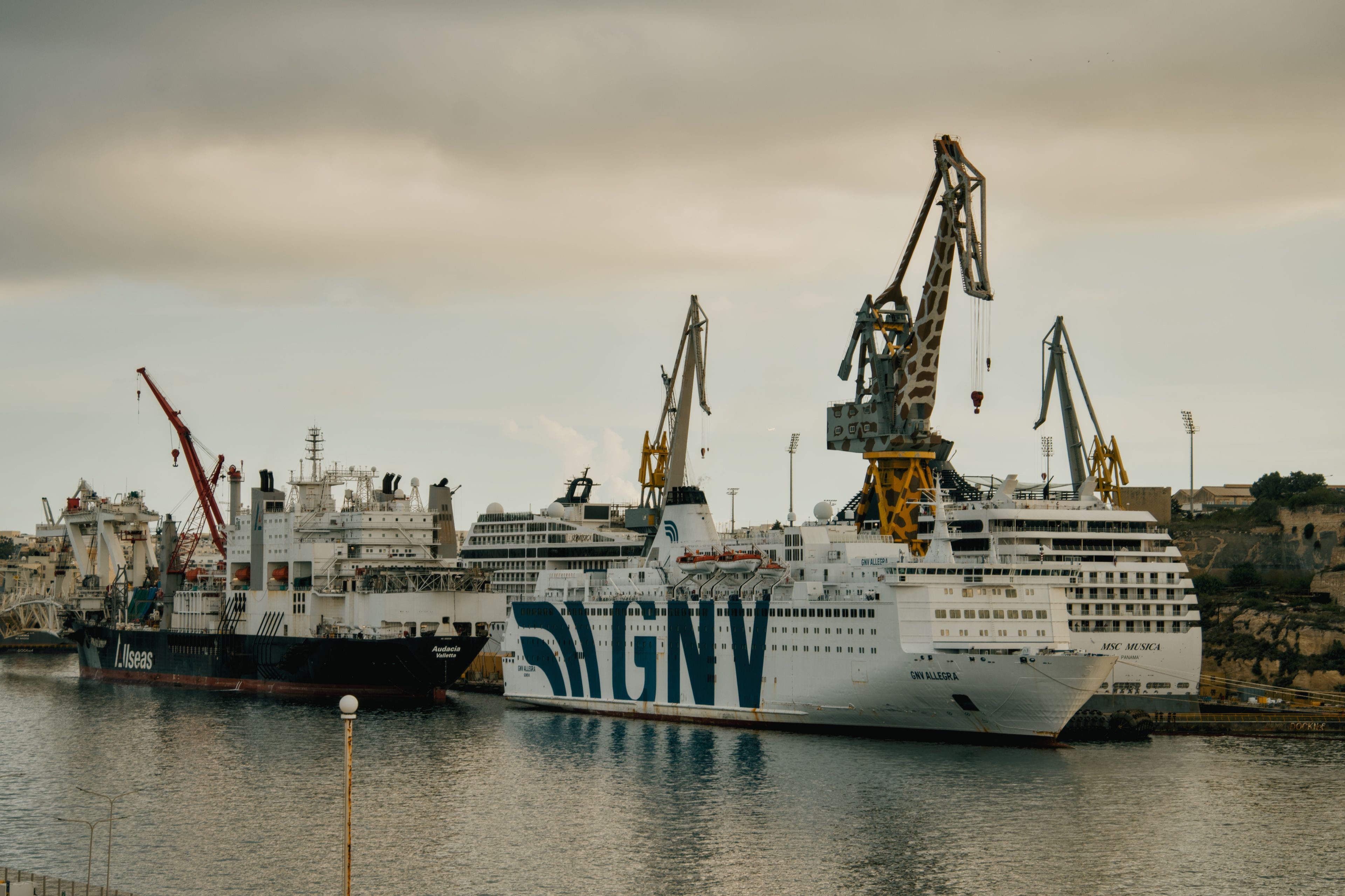 Industrial port with docked ships and cranes at Marsa, Malta under an overcast sky.