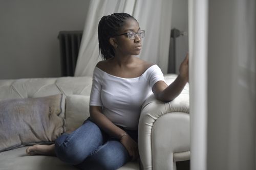 Free Woman in glasses relaxing on a sofa near window, deep in thought and looking outside. Stock Photo