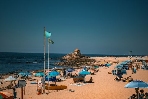 Free Beachgoers enjoy a summer day at Praia de Miramar in Porto, Portugal, with umbrellas and the iconic chapel in view. Stock Photo