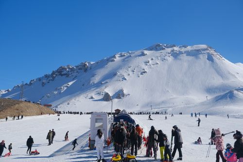 Free Crowds enjoying skiing and snowboarding in Isparta's snowy mountains under a bright blue sky. Stock Photo