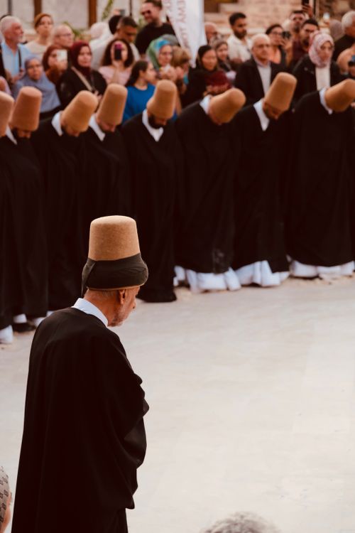 Free Sufi dervishes in ceremonial attire perform a traditional whirling dance in an outdoor setting. Stock Photo