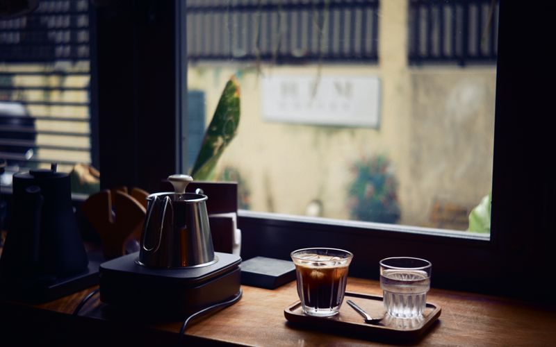 A cozy indoor cafe scene featuring a coffee and water on a wooden table by the window.