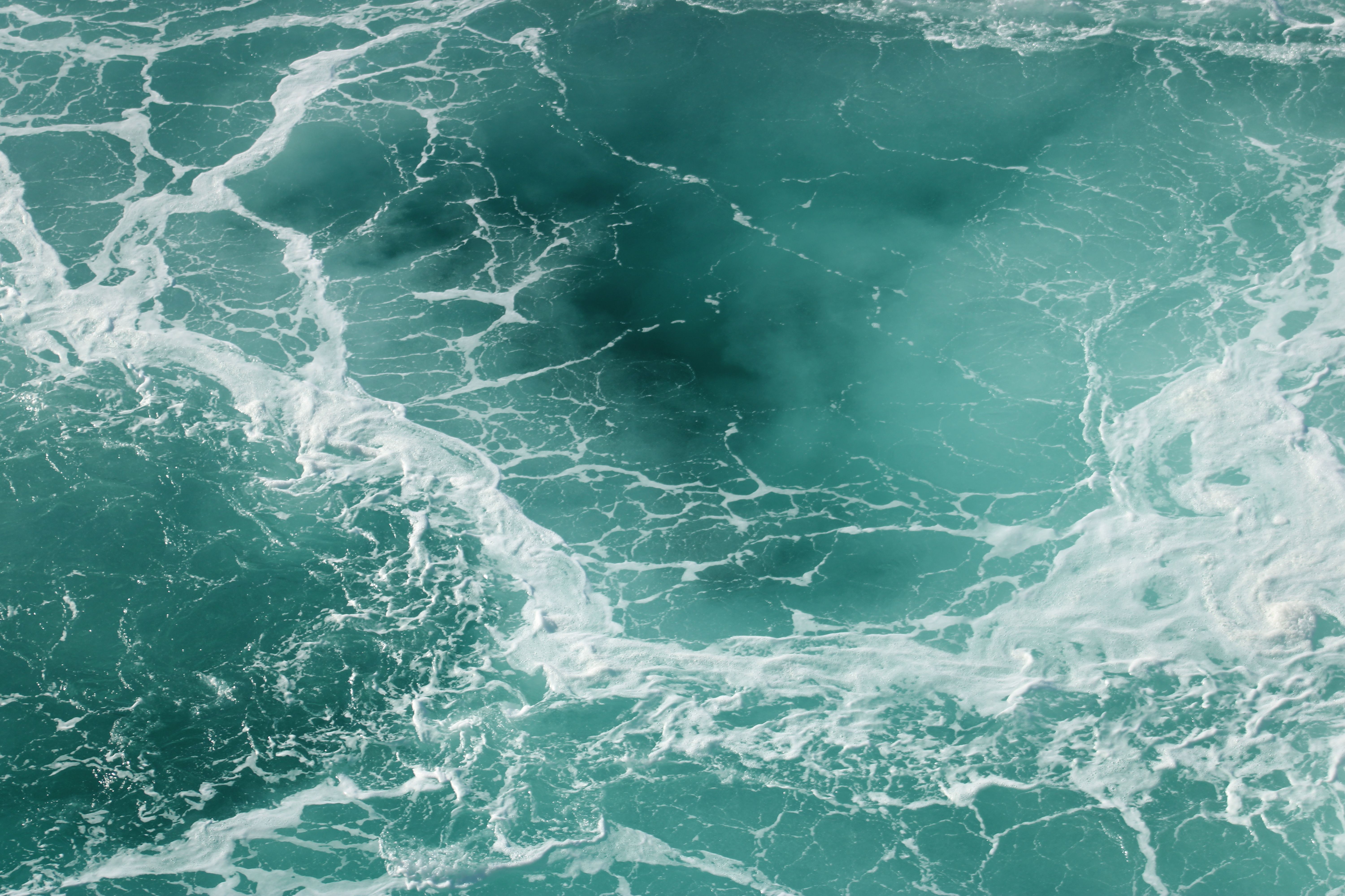 Aerial view of turquoise ocean waves, creating patterns with white foam.