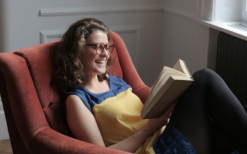 Young woman reading book while sitting on armchair at home