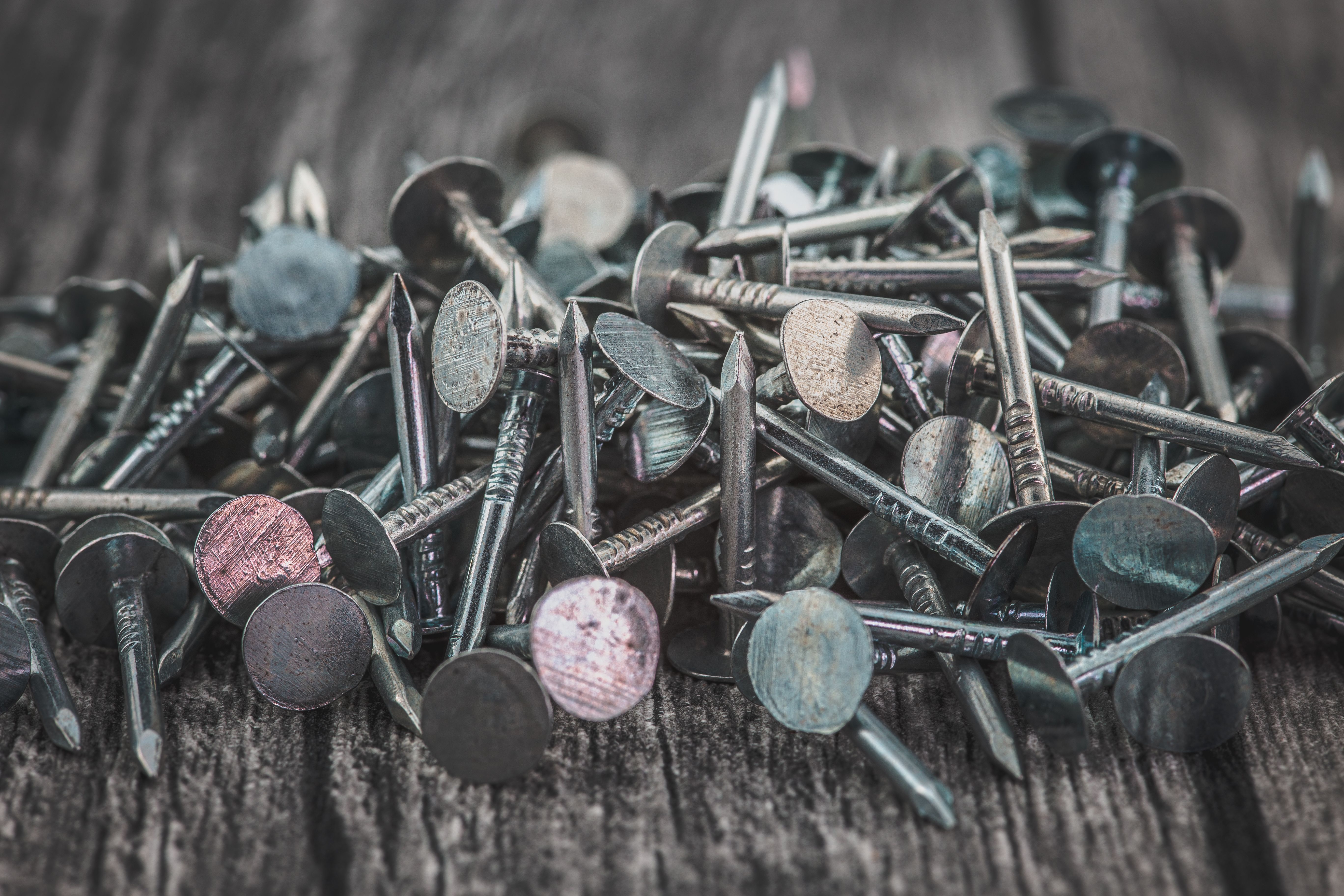 A close-up view of scattered metallic nails on a wooden surface, showcasing texture and detail.