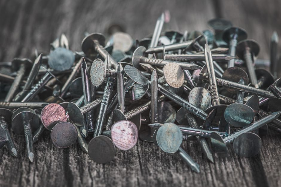 A close-up view of scattered metallic nails on a wooden surface, showcasing texture and detail.