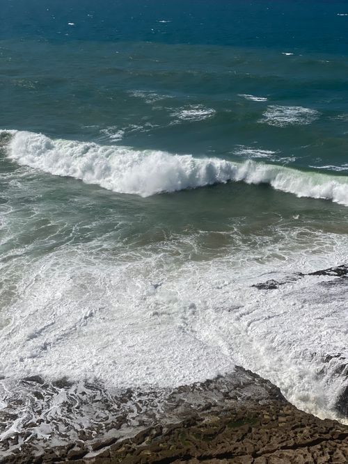 Free Powerful ocean waves crash against a rugged rocky shore under a bright sky, capturing nature's raw force and beauty. Stock Photo