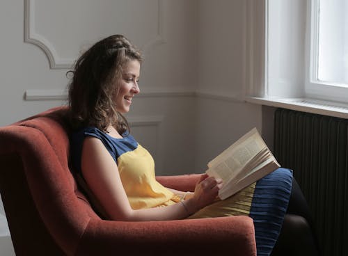 Free Woman  Reading a Book Sitting on Red Sofa Chair Stock Photo