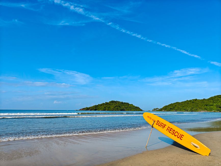 Vibrant yellow surf rescue board on a tranquil beach with clear blue skies and lush green hills.