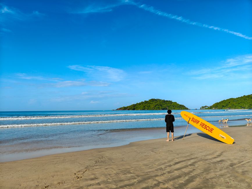 A lifeguard stands by a surf rescue board on a sunny tropical beach.