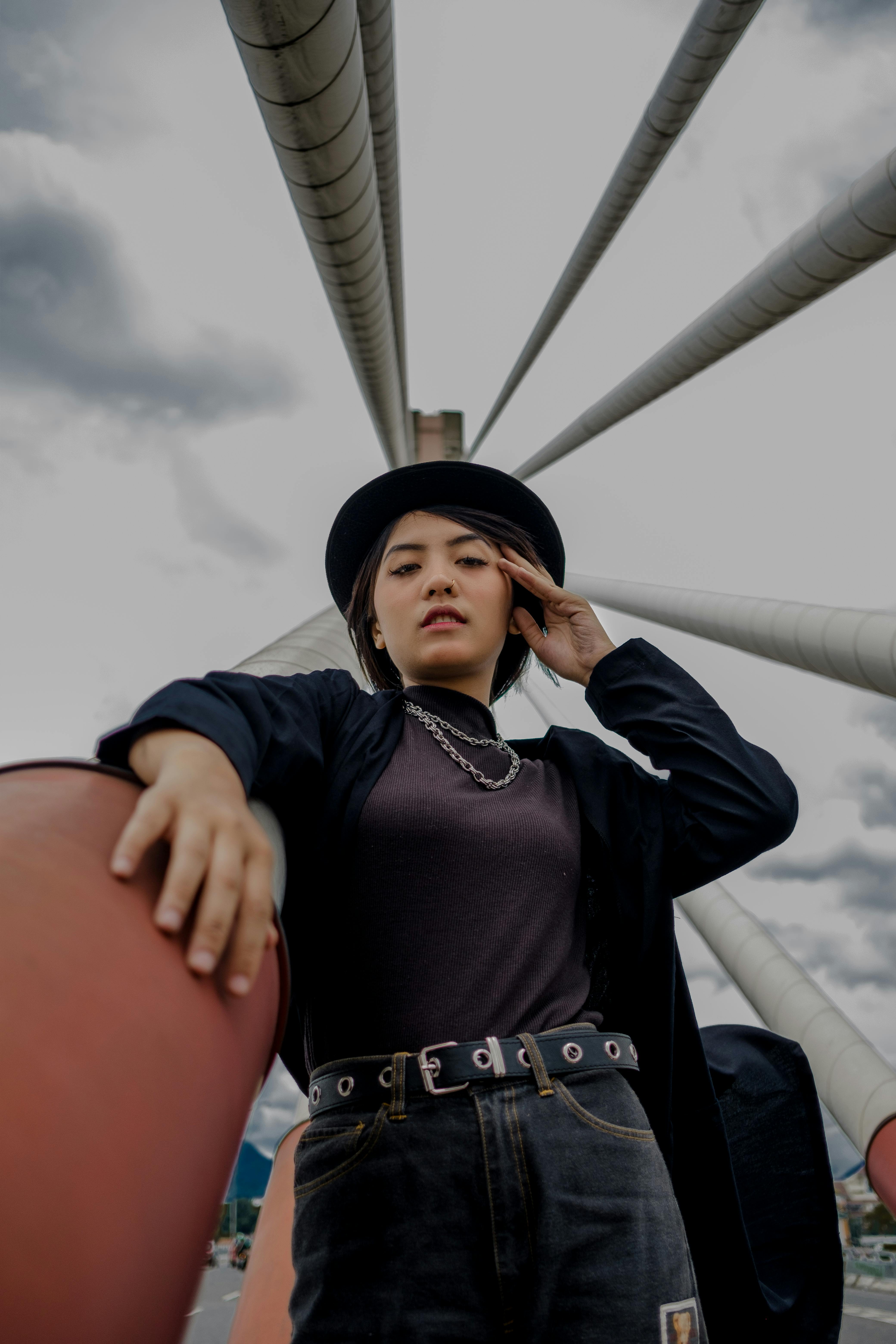 戴着帽子和夹克的时尚女人在现代吊桥上摆姿势