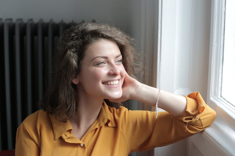 Happy Young Woman Looking Out Window At Home