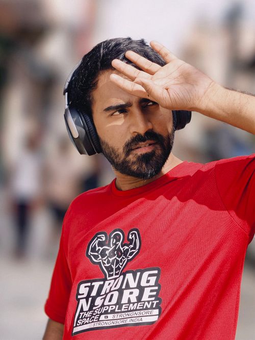 Free Man shielding eyes from sun, wearing headphones and StrongSore t-shirt outdoors. Stock Photo