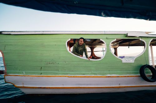 Free Man aboard a wooden boat on calm waters, showcasing nautical travel and serenity. Stock Photo