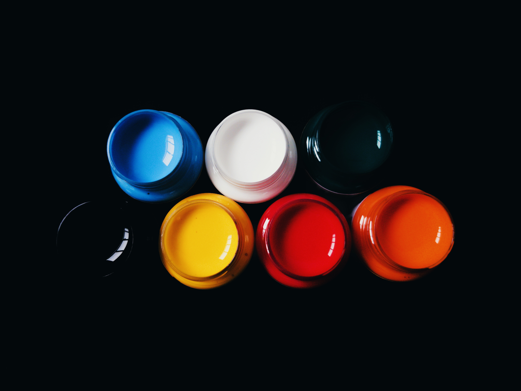 Top view of vibrant acrylic paints in jars on a black background, showcasing bold colors.