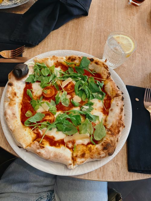 Free Mouth-watering arugula and tomato pizza served on a wooden table with fresh ingredients. Stock Photo