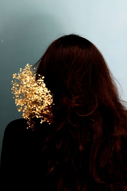 Back view of unrecognizable female with long wavy brown hair and abstract golden glitters on grey background