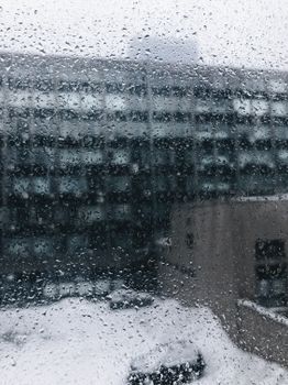 View of raindrops on a window with a snowy building backdrop highlighting winter weather.