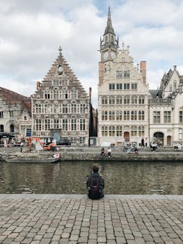 Person sitting by Ghent canal in Belgium, with view of historic architecture. by Viktor Mogilat