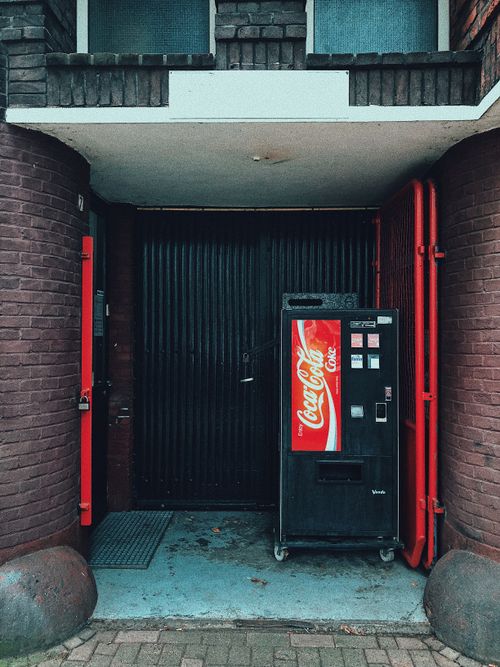 Free Vintage Coca-Cola vending machine in Amsterdam against urban brick backdrop. Stock Photo