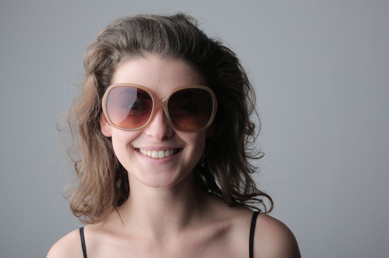 portrait of a smiling woman with wavy hair and sunglasses against a ne
