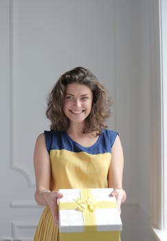 Joyful woman smiling while presenting a beautifully wrapped gift indoors.