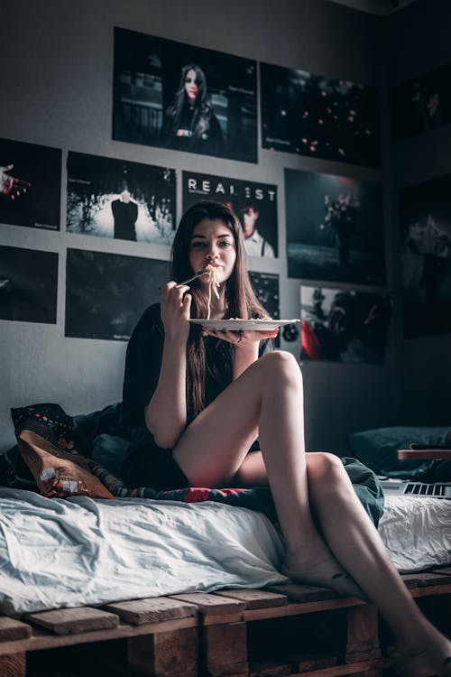 Free Woman in Black Tank Top Sitting on Bed Holding a Plate  Stock Photo