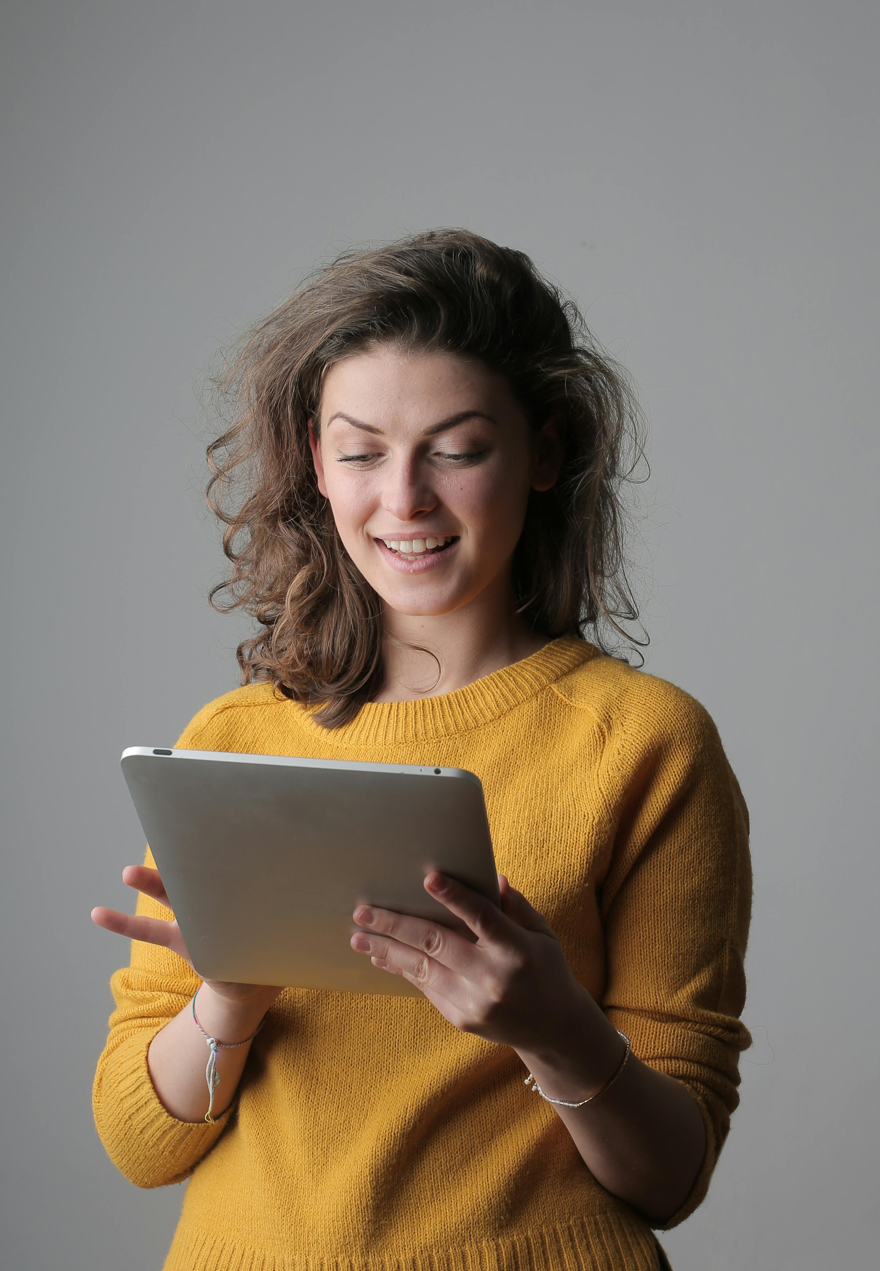 微笑的年轻女子穿着黄色毛衣，在室内使用数字平板电脑