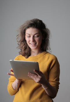 一位穿着黄色毛衣的年轻女子在室内微笑着使用数字平板电脑