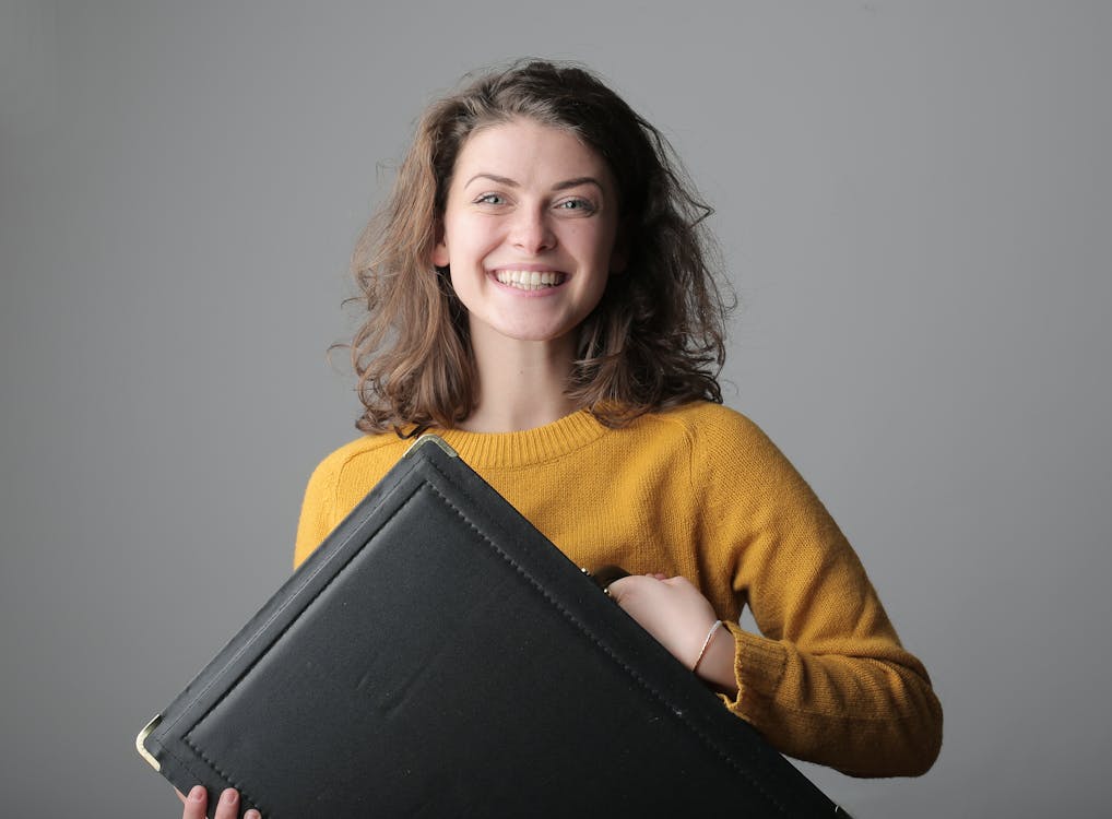 Woman in Yellow Sweater Holding Black Leather Case