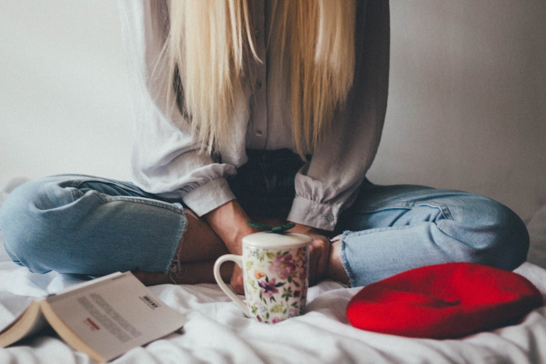 Woman Sitting On A Bed Beside Mug And Books