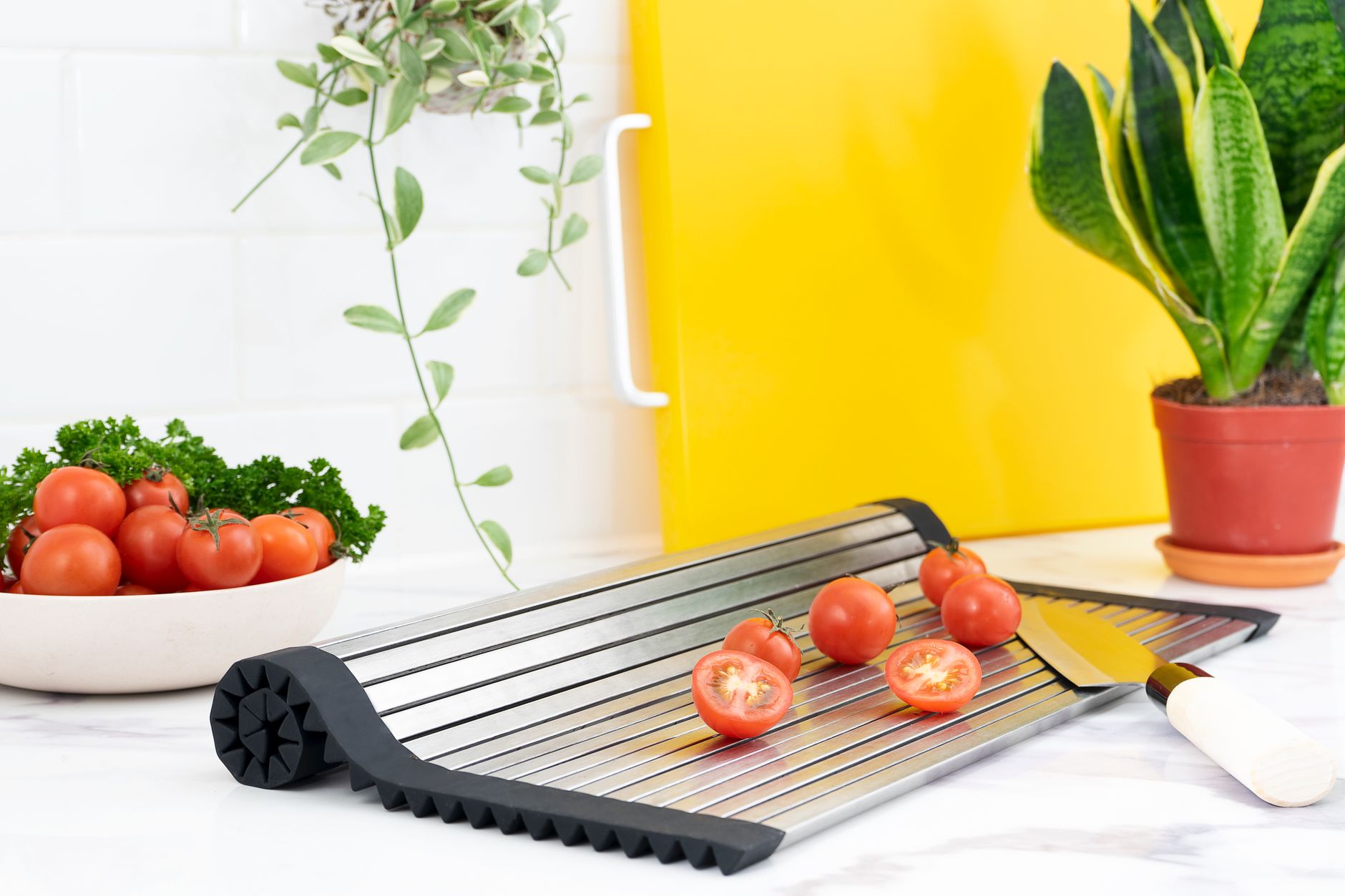 A vibrant kitchen scene featuring cherry tomatoes on a rollable cutting board with plants in the background.