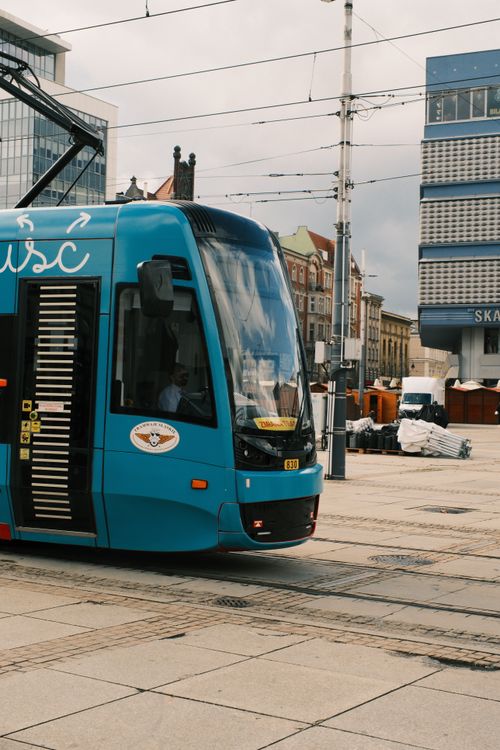 Free A sleek blue tram travels through a bustling urban environment on a cloudy day. Stock Photo