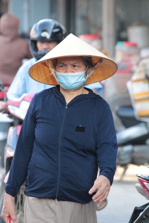 Free A senior woman wearing a traditional conical hat and face mask in an outdoor market. Stock Photo