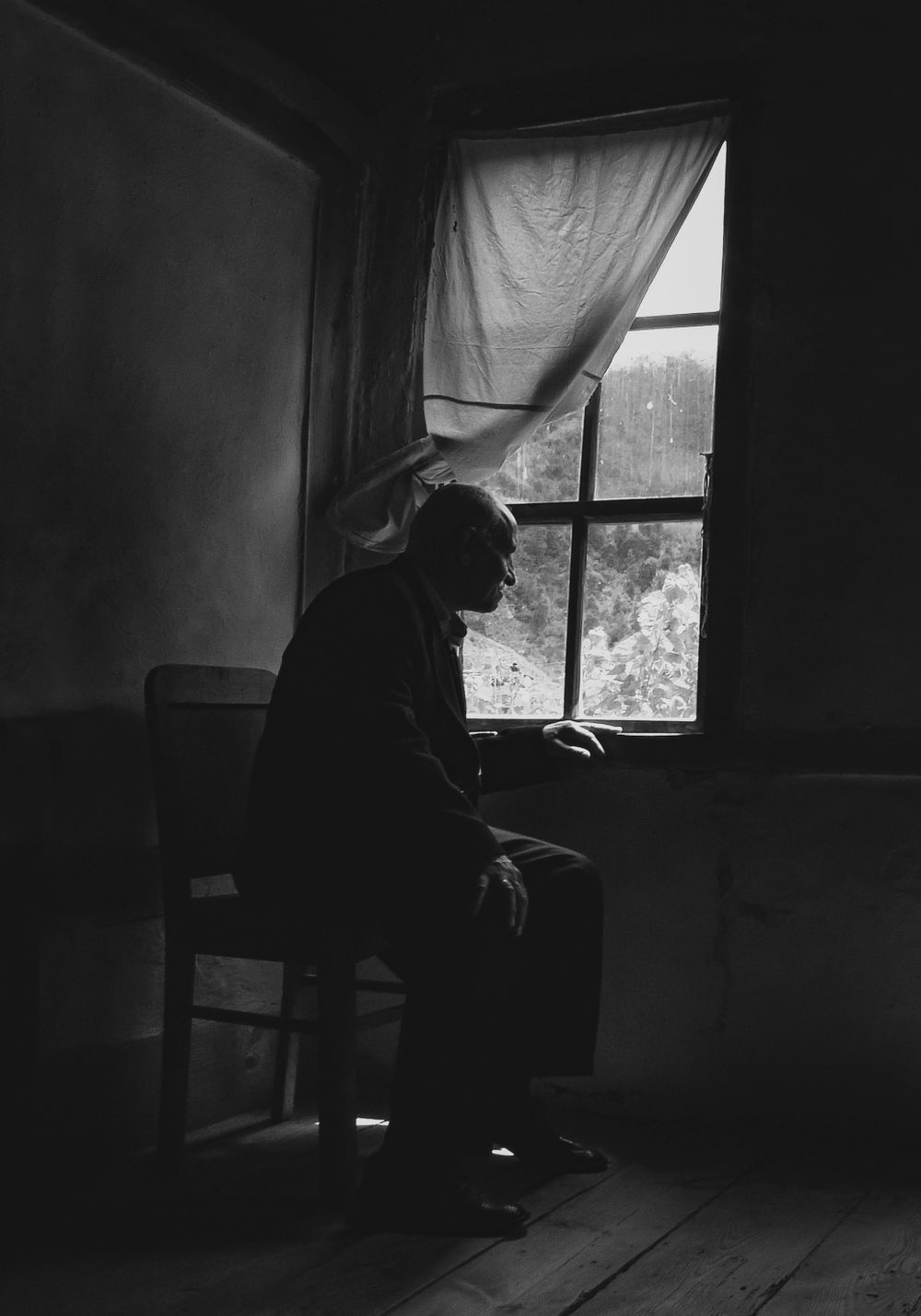 An elderly man sitting alone by a window in black and white