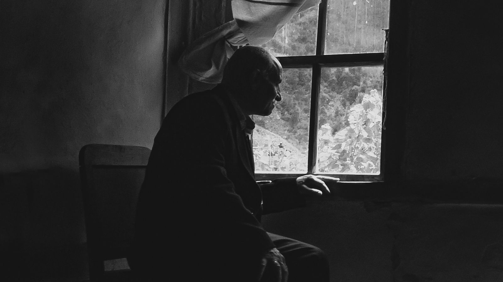 Black-and-white photograph of an adult seated beside a window
