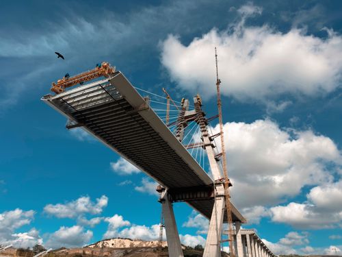 Free A partially constructed bridge extends towards the sky under a blue sky with clouds. Stock Photo