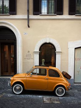 Classic orange Fiat 500 parked in front of Casa Monti on a cobblestone street in Rome, Italy.