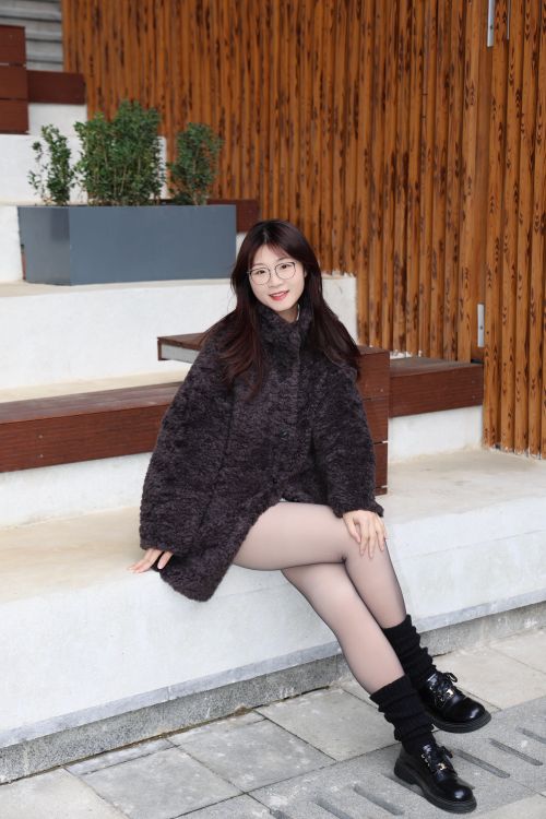 Free Stylish young woman in glasses and wool coat sitting outside in Hefei. Stock Photo
