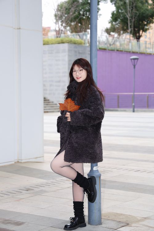 Free Young woman with glasses in a cozy coat holding a fall leaf outdoors. Stock Photo