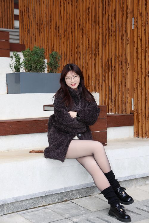 Free Young woman in cozy winter attire sitting on outdoor urban stairs in Hefei, China. Stock Photo