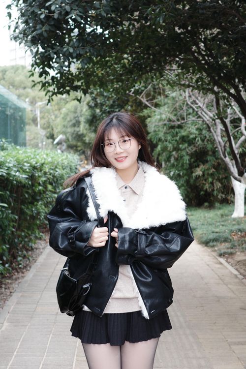 Free A young woman walks outdoors wearing a fashionable black leather coat with a faux fur collar, exuding a casual, trendy look. Stock Photo