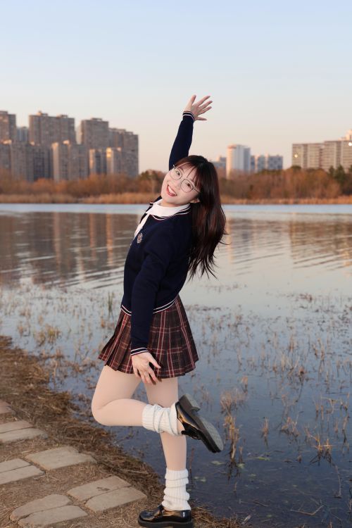 Free Cheerful young woman in school uniform posing by a lake at sunset in Hefei, China. Stock Photo